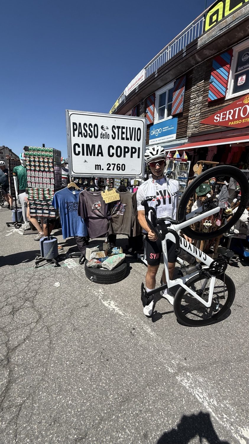Holding a white road bike overhead next to the Passo dello Stelvio summit sign, 2760 m